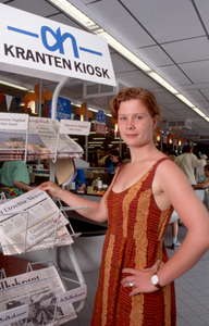 846321 Afbeelding van een jonge vrouw die de krant Het Utrechts Nieuws pakt uit het krantenrek van supermarkt Albert ...